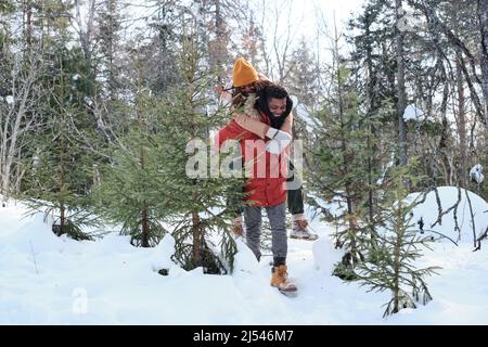 Cheerful young Black man in love giving his girlfriend piggyback ride while hiking in mountains on winter day Stock Photo