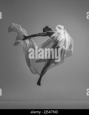 Liberty. Black and white portrait of graceful muscled male ballet dancer dancing with fabric, cloth isolated on grey studio background. Grace, art Stock Photo