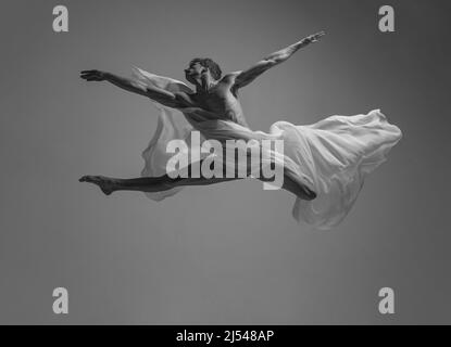 Desire. Black and white portrait of graceful muscled male ballet dancer dancing with fabric, cloth isolated on grey studio background. Grace, art Stock Photo