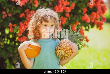 Child boy holding pineapple and coconut smiling with happy face in yard. Summer fruits Stock Photo