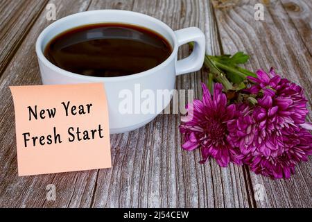 Text written on sticky note with white coffee cup and flowers - New year fresh start. New year concept. Stock Photo