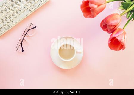 Pink female workplace with keyboard, tulip flowers, coffee cup and glasses. Spring holidays, mothers day concept. Top view, flat lay Stock Photo