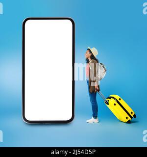 Black Tourist Female Near Cellphone Looking At Screen, Blue Background Stock Photo