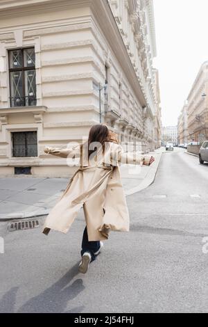 back view of woman in trench coat walking on street of european city ...