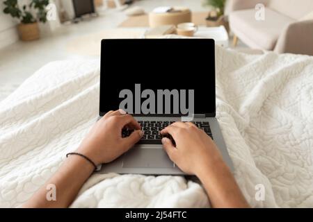 Cropped Shot Of Man Using Laptop Working Lying In Bedroom Stock Photo