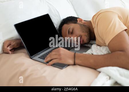 Tired Middle Eastern Male Freelancer Sleeping Near Laptop In Bedroom Stock Photo
