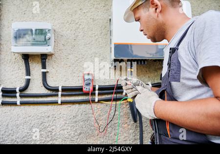 Man electrician installing solar panel system. Inspector in gloves making electrical wiring inverter and electric box. Concept of alternative and renewable energy. Stock Photo