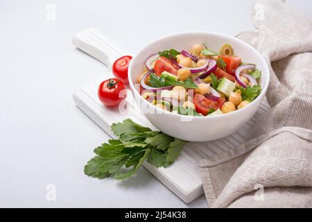 Healthy and tasty vegan food. Chickpea salad with parsley, cherry tomatoes, onion, cucumber and green olives on grey concrete background Stock Photo