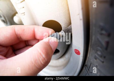 The auto mechanic hand puts on the tire valve cap of a car wheel Stock Photo