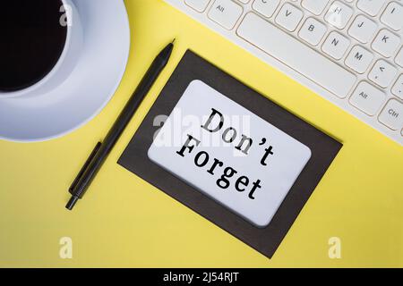 Don't forget text on white note with keyboard, pen and coffee cup on yellow background. Stock Photo
