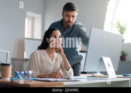 Young female trainee working on computer together with her business mentor at modern company office Stock Photo