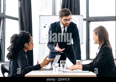 Cooperation, business brainstorm of multiracial partners in modern office, intelligent attractive caucasian man discuss financial strategy to female partners, analyzes report and profit, explain info Stock Photo