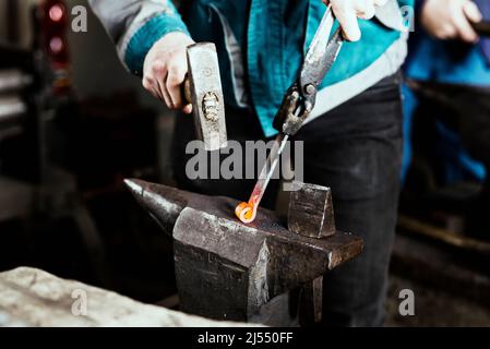 Blacksmith forges hinge on a anvil. Hammering hot red steel Stock Photo
