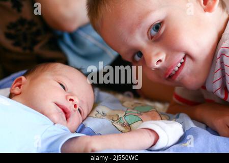 Two weeks old newborn boy infant with anti grasping gloves meets with his four years older brother Stock Photo