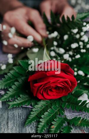 closeup of a young caucasian man arranging a bouquet of flowers with some red roses, on a gray rustic worktop Stock Photo