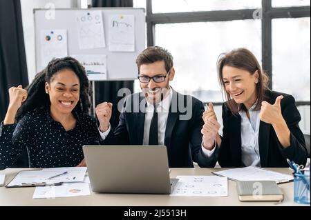 Win, triumph. Joyful creative business partners working together. Multiracial colleagues are brainstorming on strategy together, sitting in modern office, using laptop, get good deal, profit,smile Stock Photo