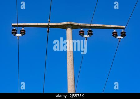 Power lines and insulators on a medium voltage concrete pole against a blue sky Stock Photo