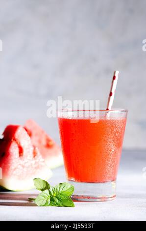 A glass of watermelon juice, slices of watermelon fruit and mint leaves on a grey background. Front view. Stock Photo