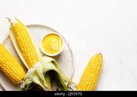 Three corncobs, and a bowl with cornmeal in a plate on a white background. Stock Photo