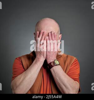 casual portrait of a senior bald man covering his face with hands, tired, stressed or in dispair Stock Photo
