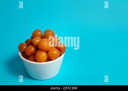 White cherries unfrozen in white cup on blue background Stock Photo