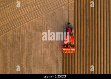 PRAGUE , CZECH REPUBLIC - MARCH 18 2022: Tractor drives preparing beds for planting seedlings in cultivated soil. Heavy machine tills on field helping with agriculture aerial view Stock Photo