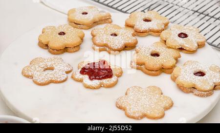 Flower-shaped shortbread cookies filled with raspberry jam step by step recipe. Spreading a layer of raspberry jam on baked cookies Stock Photo
