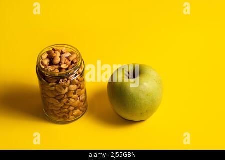 Peanuts in a glass jar and green apple on a yellow background Stock Photo