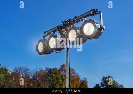 Street spotlight. Four round glowing lamps. Lighting of streets, objects, buildings. Blurred background of sky and trees Stock Photo