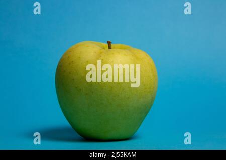 Big green apple over blue background. Golden Delicious apple Stock Photo