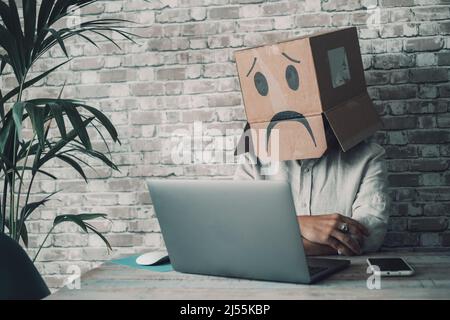 Depression and problems working alone at home in smart work modern job. Woman with sad carton box covering head looking her laptop computer. Password Stock Photo