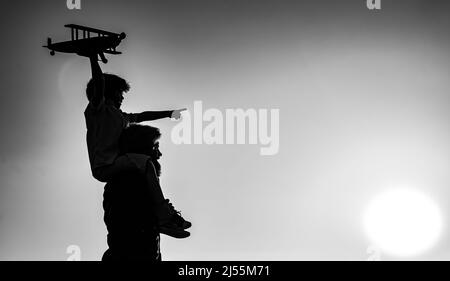 Success and child leader concept. Sunset silhouette of Father and son together. Boy child is sitting on daddy shoulder piggyback while the flight. Stock Photo