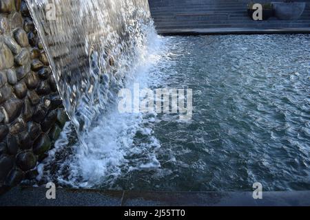 A waterfall flowing at park. A waterfall of a fountain in a garden. Wall of water. A beautiful view of the falling water cascade. Artificial waterfall Stock Photo