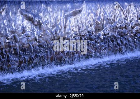 A waterfall flowing at park. A waterfall of a fountain in a garden. Wall of water. A beautiful view of the falling water cascade. Artificial waterfall Stock Photo