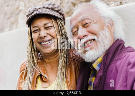 Multiracial senior couple doing selfie with mobile phone outdoor - Focus on african woman face Stock Photo