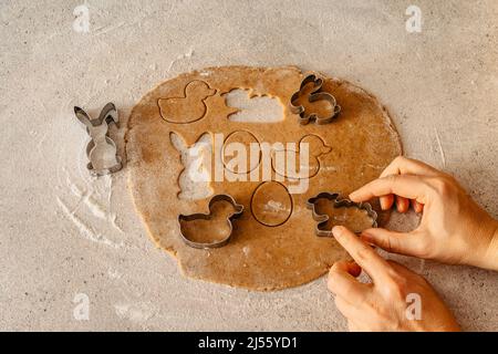 Process of making gingerbread biscuits on table full of flour.Woman hands preparing Easter cookies from honey dough.Easter bunny,rabbit,eggs and ducks Stock Photo