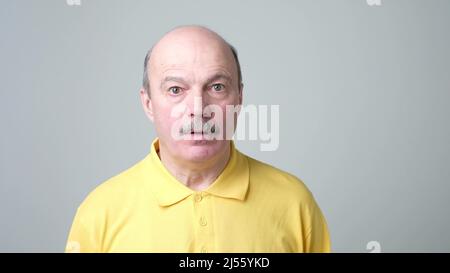 Shocked senior man in yellow shirt is surprised with news he head. Stock Photo