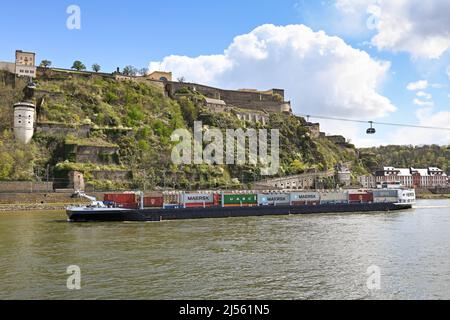 Koblenz, Germany – April 2022: Industrial barge transporting shipping containers on the Rhine River passing underneath cable cars Stock Photo
