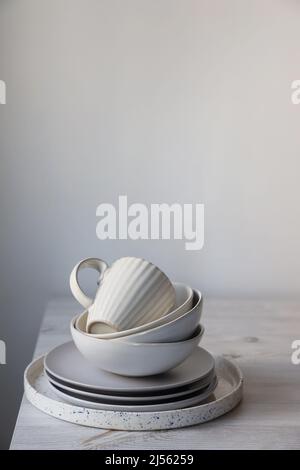 A pyramid of white bowls, plates and cups of different sizes and colors on a beige table in the kitchen. Scandinavian style. Place for your text. Copy Stock Photo