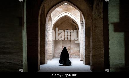 Isfahan, Iran - May 2019: Unidentified iranian woman in hijab black dress walking along the ancient columns of Jameh Mosque of Isfahan Stock Photo