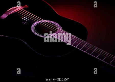 black guitar on a dark background under beam of red light. guitar music low-key concept Stock Photo