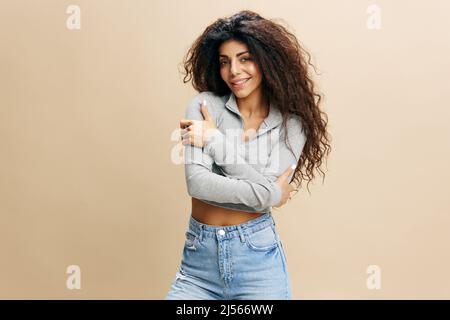 GOOD OFFER. Happy enjoyed pretty Latin female with afro folded arms, crossing hand, hugging herself, laughing, stay isolated over yellow background Stock Photo