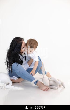 Vertical photo of serious barefoot mother holding and kissing sad son with asperger syndrome. Traumatic experience. Stock Photo