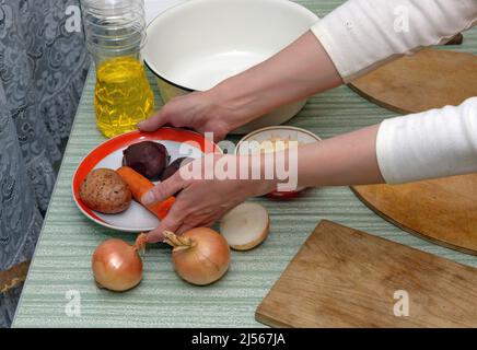 Top of kitchen table with kitchenware arranging for cooking salad and hands of woman that is putting saucer with vegetable. Stock Photo