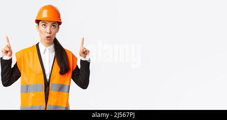 Building, construction and industrial concept. Surprised and curious asian female construction manager, engineer in safety helmet and reflective Stock Photo