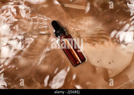 A brown bottle with a dropper floating over the water on a brown background in a top view Stock Photo