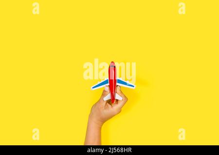 Woman hand holding a red toy plane on a yellow background with copy space Stock Photo