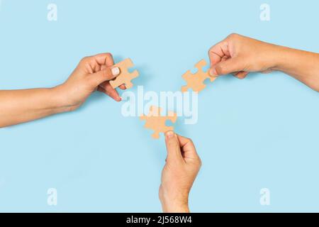 Woman and men hands holding puzzle pieces on a light blue background with copy space Stock Photo