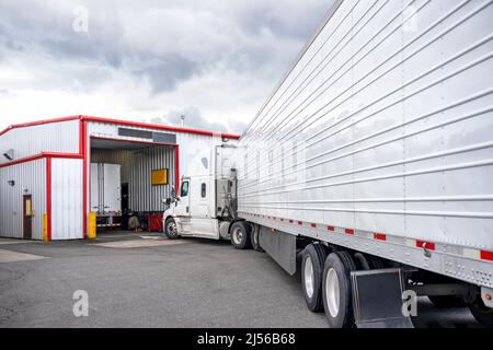Industrial standard white big rig semi truck tractor with refrigerator semi trailer standing in line to truck repair and maintenance workshop to check Stock Photo