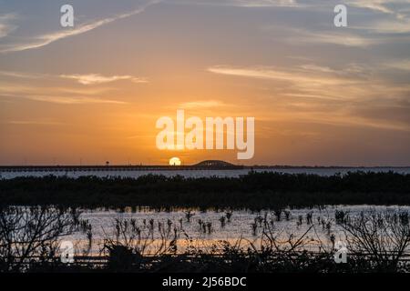 The Port Isabel Lighthouse in front of the setting sun with the Queen Isabella Memorial Bridge to the right.  Texas.  Viewed across the Laguna Madre f Stock Photo